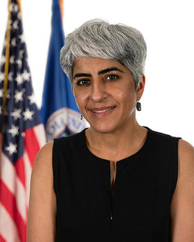 A woman with silver hair and in a black sleeveless top gazes at the camera.